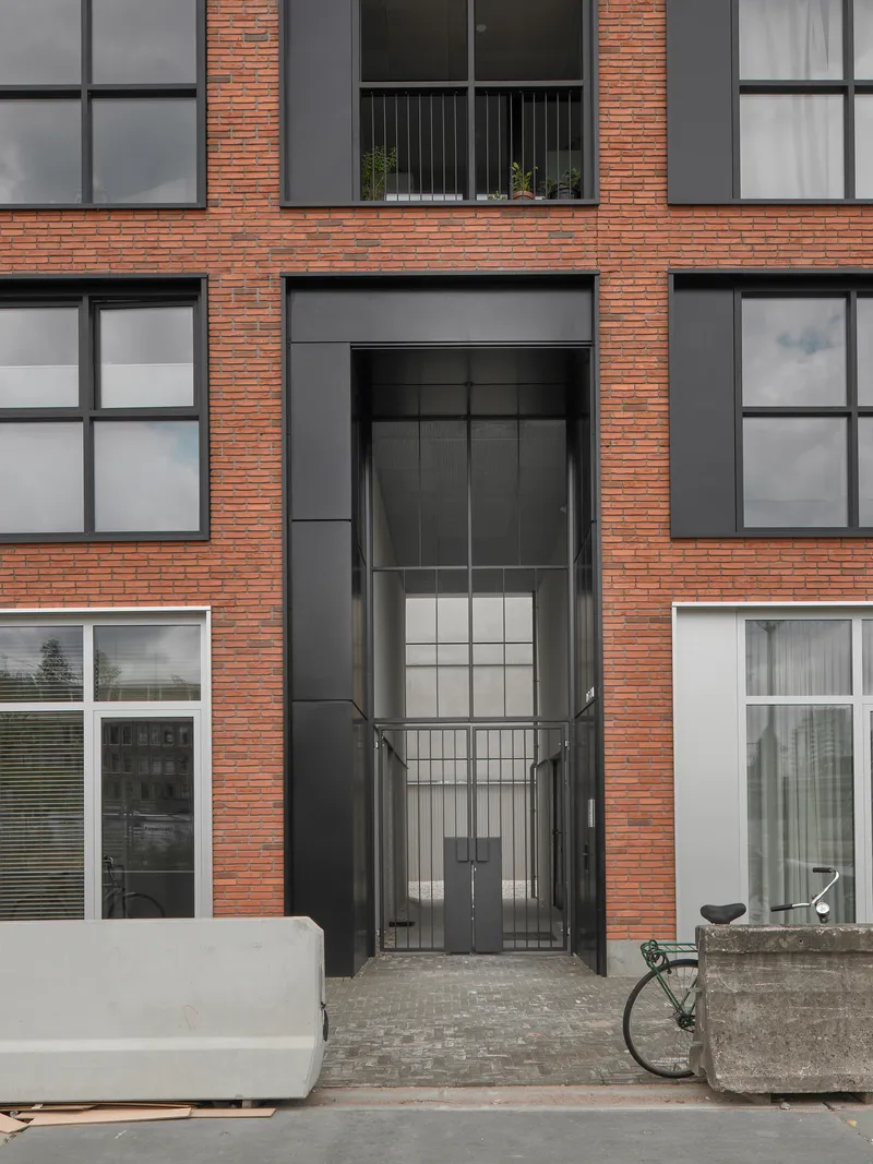 Entrance with black metal gate and frame set into orange brick facade with bicycle parked alongside