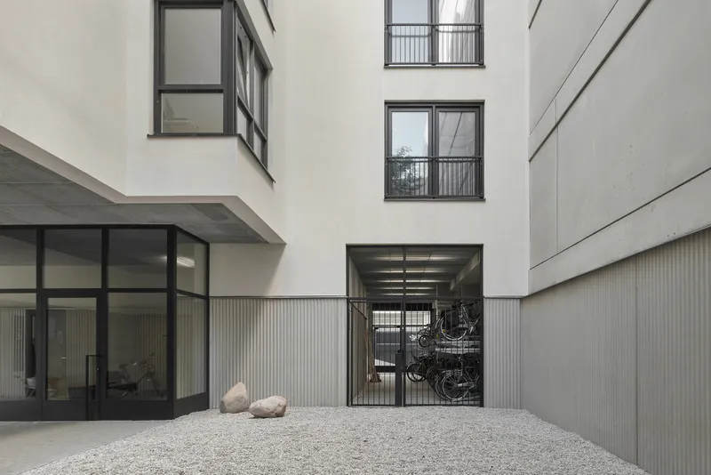 Courtyard with gravel surface, bicycle storage gate, and white rendered walls rising to the sky