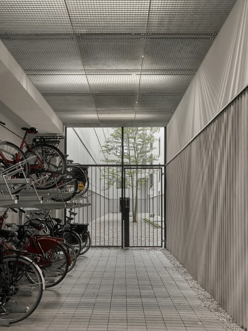 Covered bicycle storage with metal mesh ceiling and glazed gate opening to trees beyond