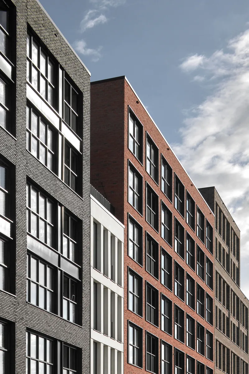 Multi-story facade with alternating bands of grey, white, and terracotta brick under a cloudy sky