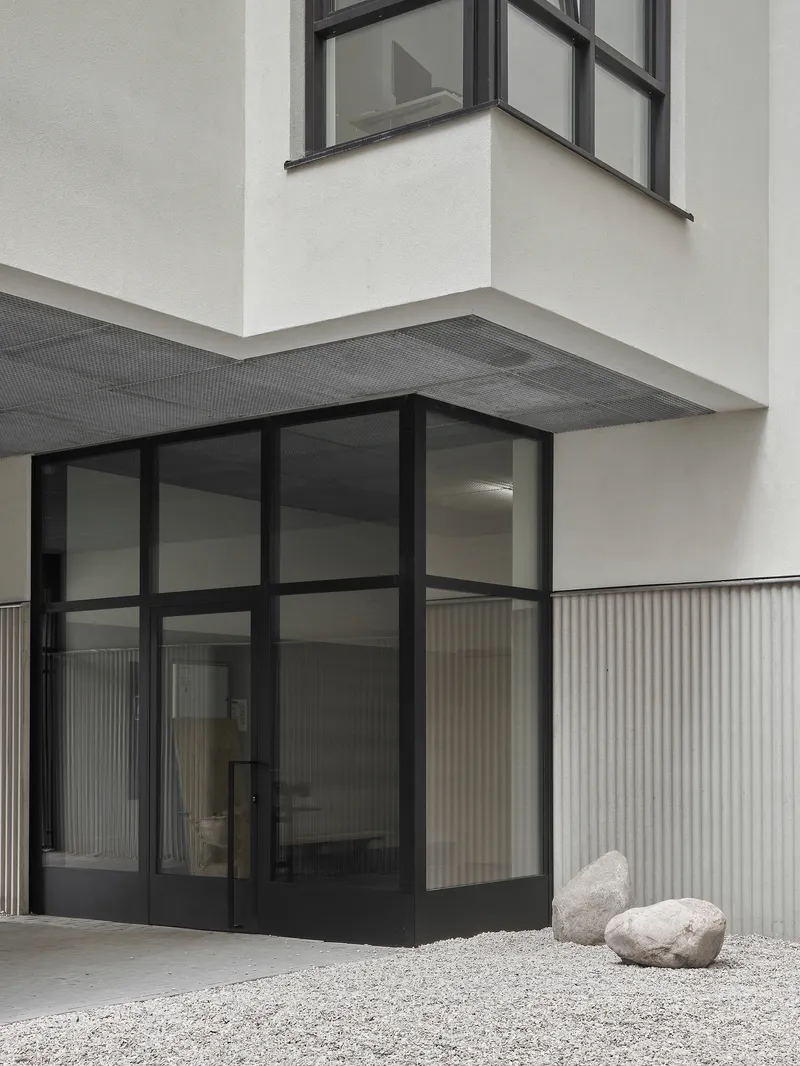 Corner entry detail showing black-framed glass doors, vertical corrugated cladding, and overhanging volume above