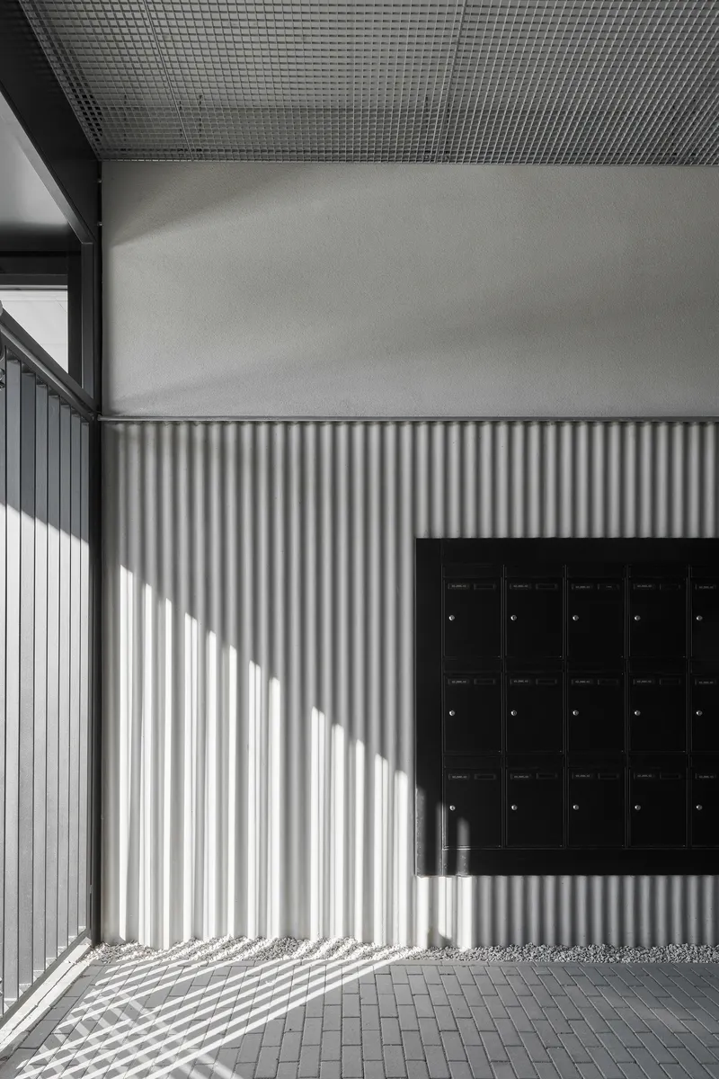 Entry alcove with corrugated metal wall casting striped shadows beside a black mailbox bank