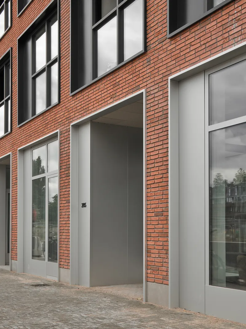 Street-level view of red brick facade with white-framed doorways and windows on a cobbled sidewalk