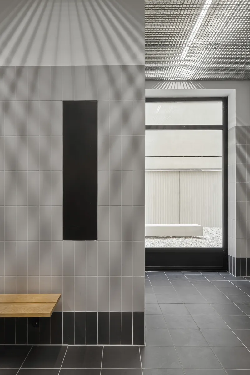 Interior entryway with grey tiled walls and ribbed metal ceiling catching dappled sunlight