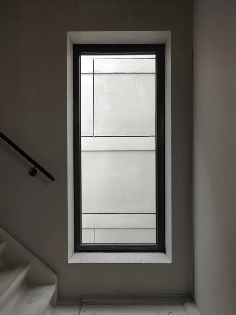 Tall window with black frame and minimal mullions beside a staircase handrail