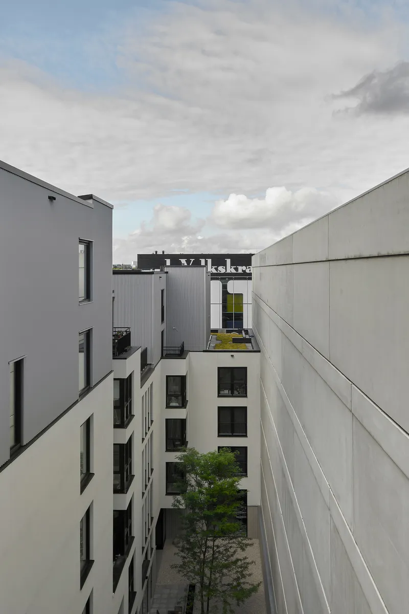 Courtyard view between white and grey facades with a young tree under cloudy skies