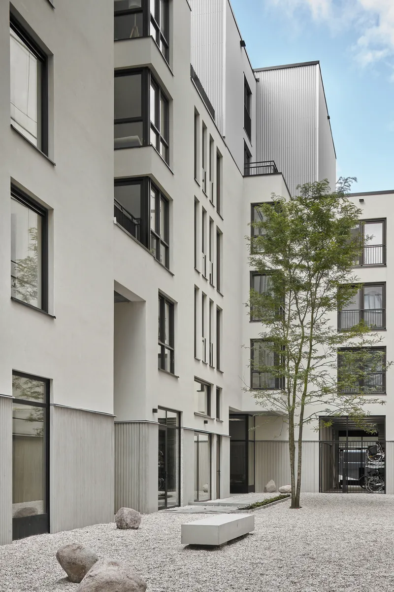 Interior courtyard with white facades, a single tree, concrete bench, and gravel ground