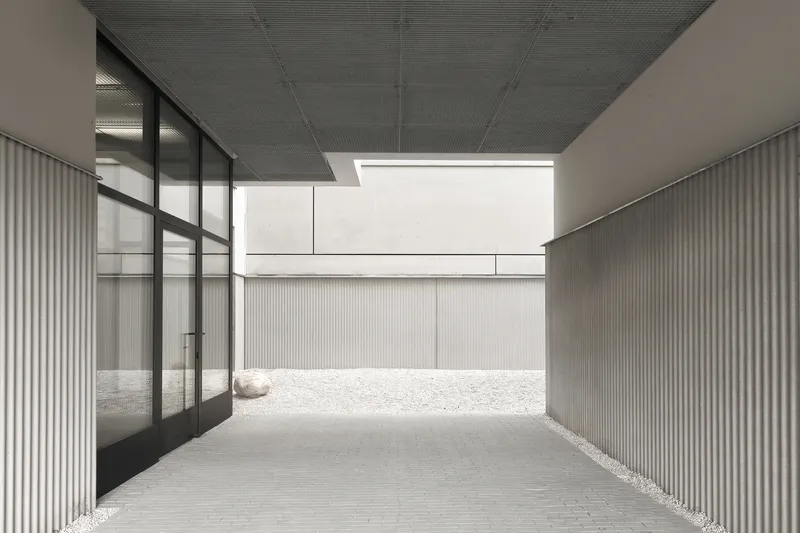 Covered passage with ribbed ceiling and glass wall opening to a gravel courtyard beyond