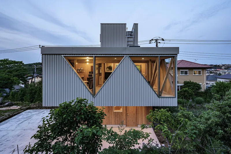 Upper level facade with triangular glazed openings illuminated at dusk framed by overhead power lines