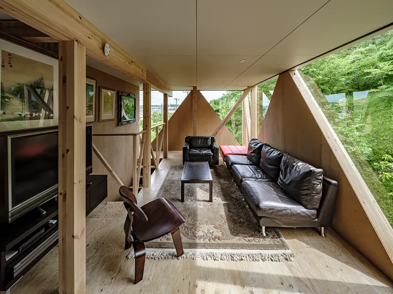 Interior living space with exposed timber columns and plywood walls framing views to surrounding greenery