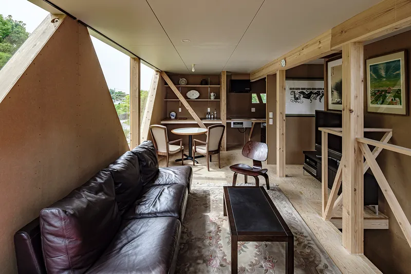 Interior living space with angled timber braces, built-in shelving and view through triangular window opening