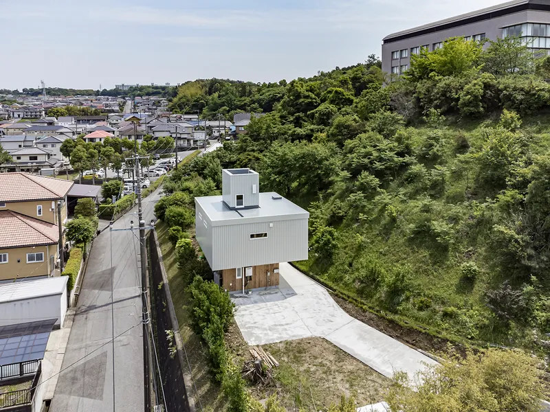 Aerial view of a white metal-clad house with a rooftop tower set on a sloping site above a residential neighborhood