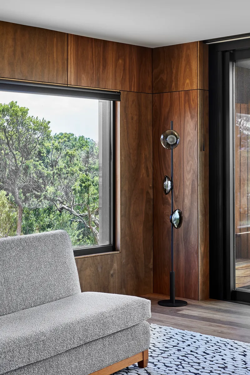 Living room corner with timber-paneled walls and black-framed window framing native trees