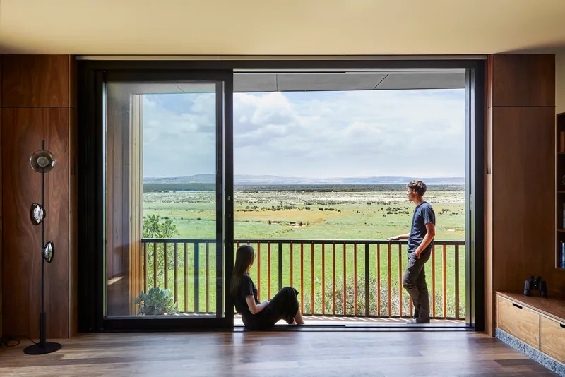 Open glass door with two figures on the threshold framing a vast grassy plain