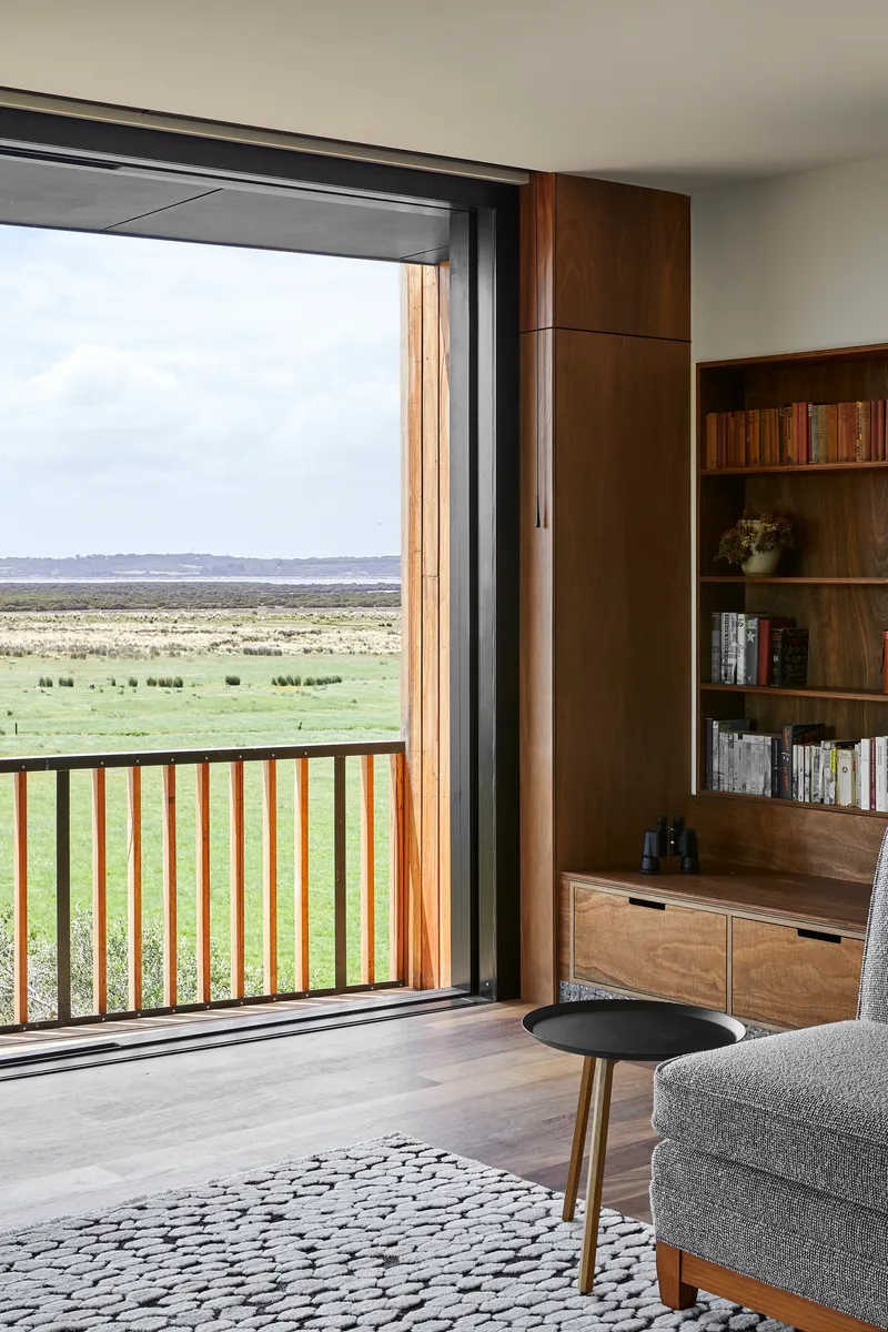 Living room with timber bookshelf beside sliding door opening to a timber-railed balcony