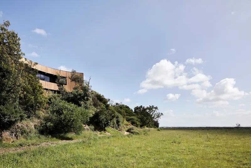 Timber structure nestled into a hillside covered in dense vegetation above an open grassy plain