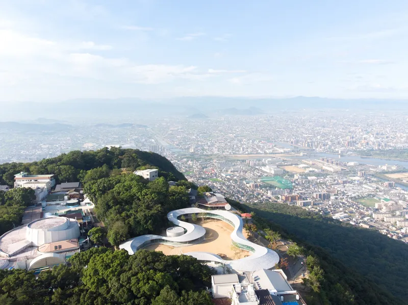 Drone perspective of the undulating roof form on a hilltop with sprawling valley cityscape beyond