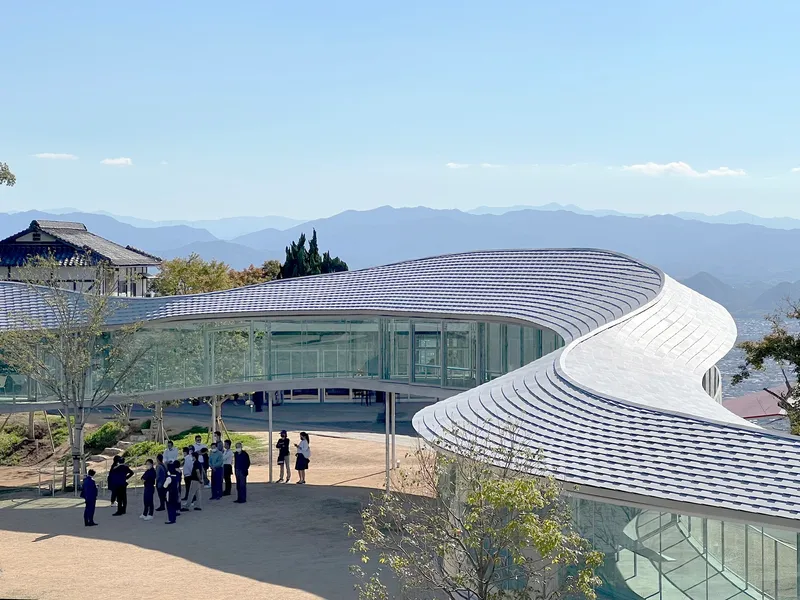 Ribbed white roof canopy over continuous glass walls with visitors gathered on the forecourt