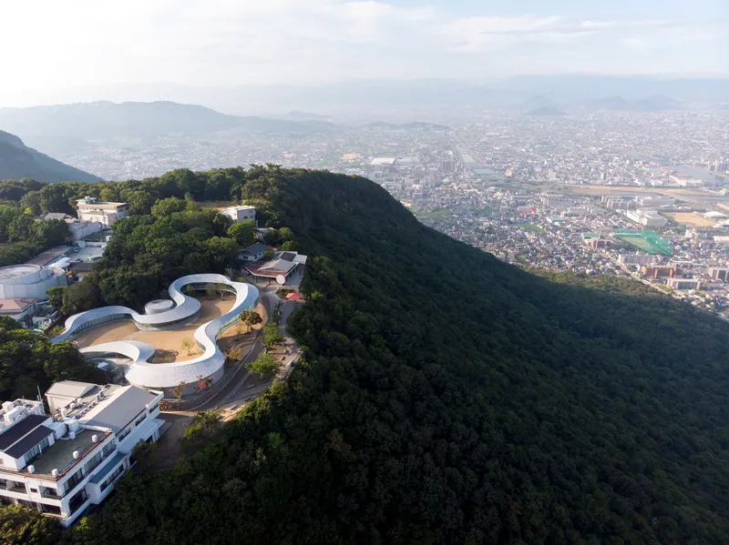 Elevated view of the curved roof volumes perched on a wooded ridge above the urban plain