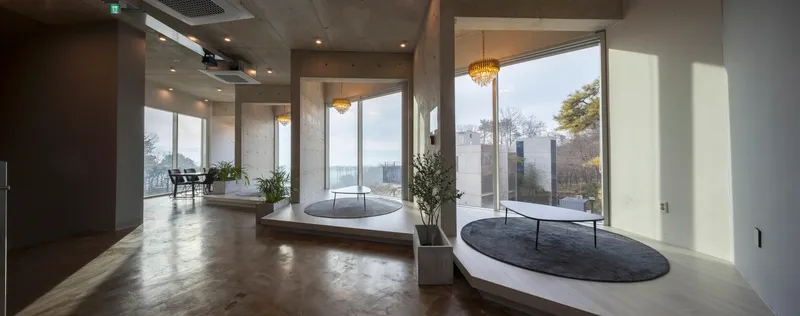 Interior corridor with polished concrete floors, circular recessed seating platforms, and glazed walls opening to the hillside