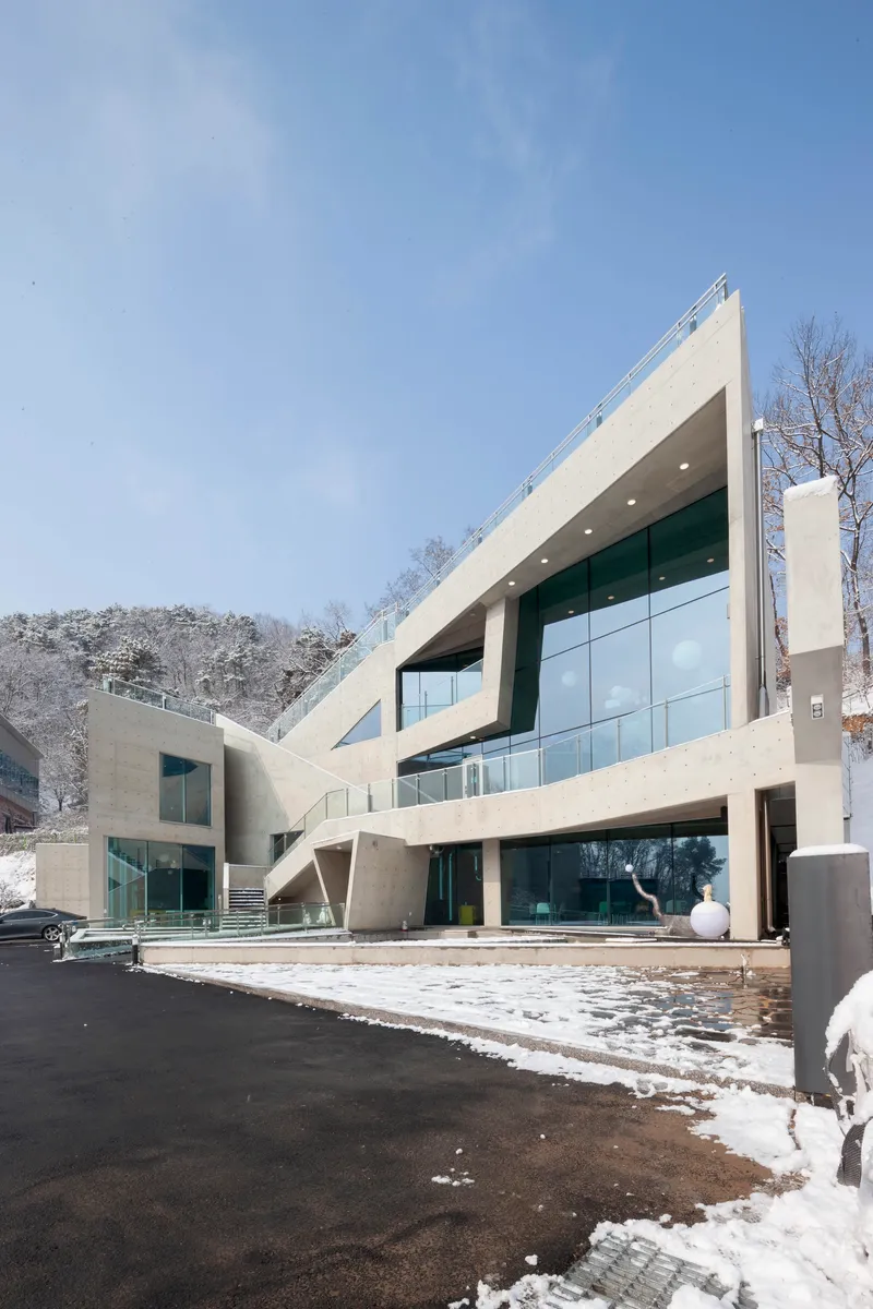Entry facade with cantilevered concrete slabs and curtain wall glazing under clear blue sky with melting snow