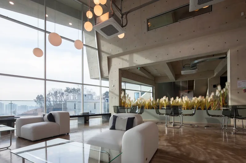 Double-height lobby with concrete ceiling, floor-to-ceiling glazing and pendant lighting above seating