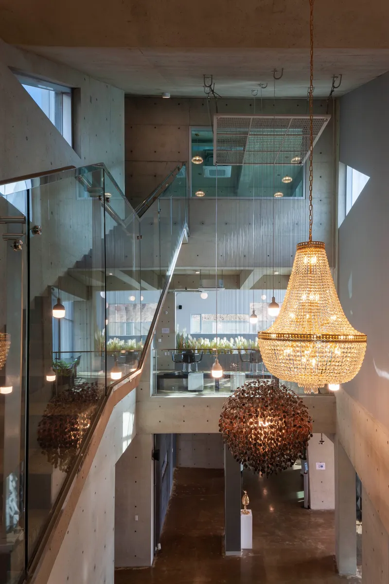 Multi-story atrium with concrete walls, glass balustrades and suspended chandeliers filtering daylight