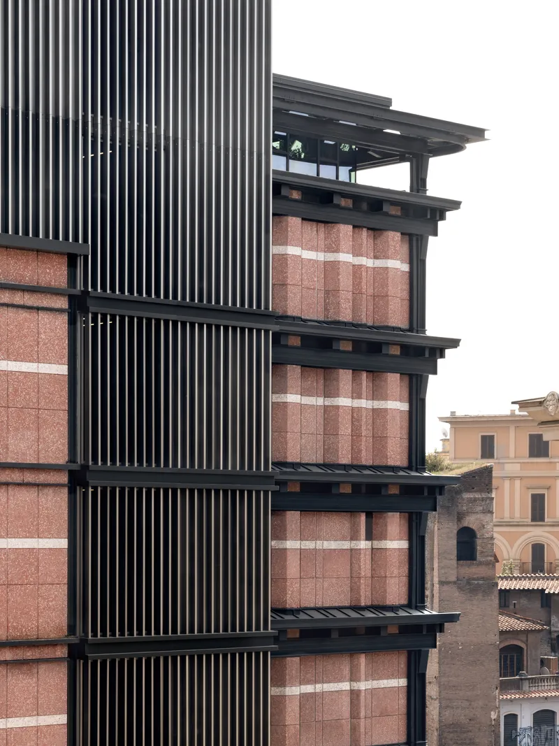 Facade detail showing black vertical louvres alternating with terracotta tile panels and projecting floor slabs