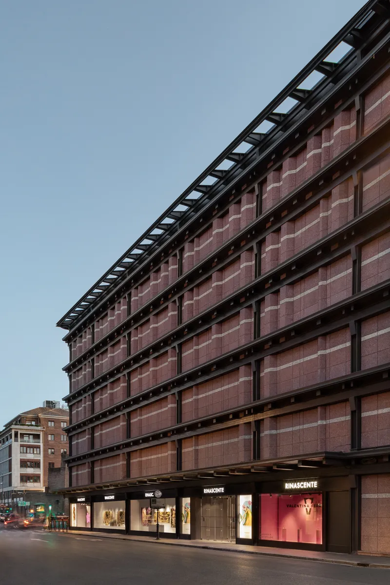 Street elevation with terracotta tile curtain wall and black structural frame at dusk