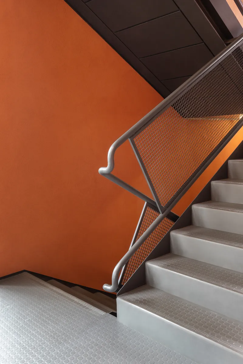 Staircase with perforated metal balustrade and terrazzo treads against an orange wall