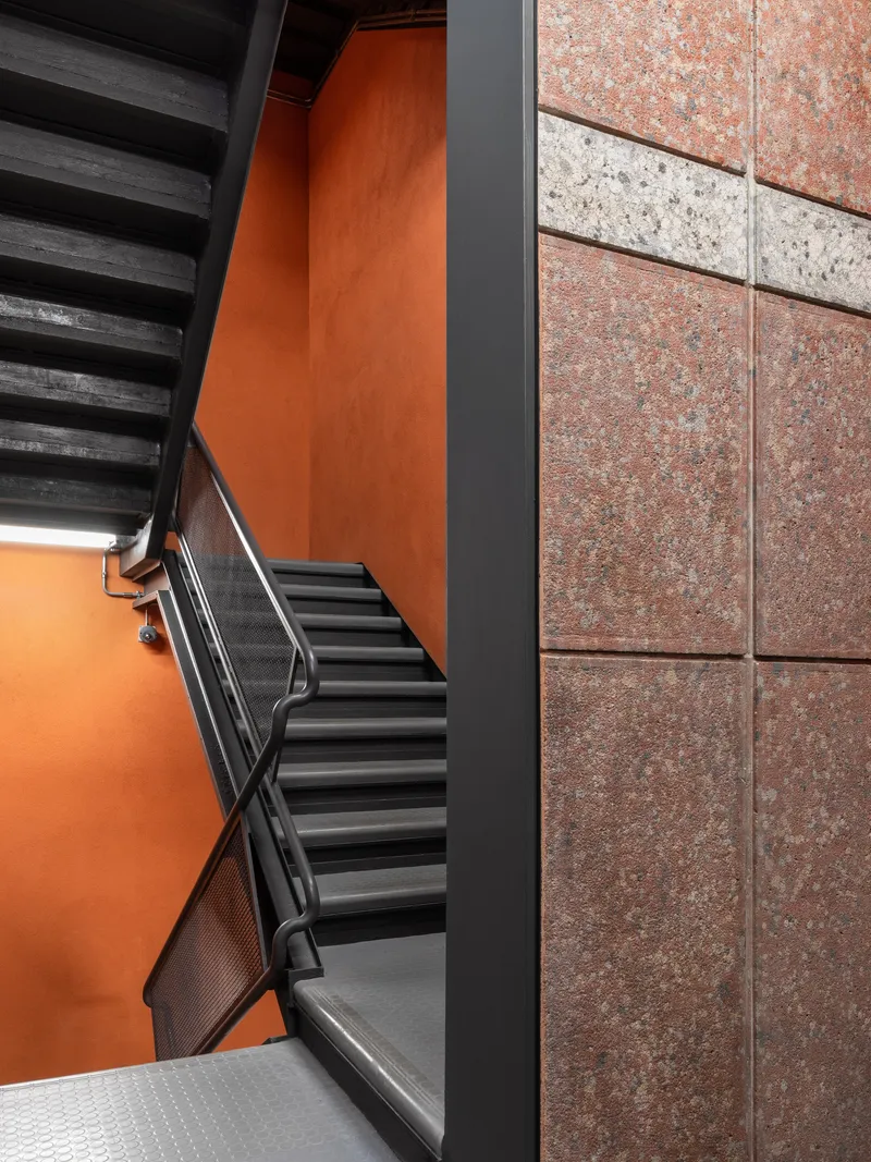 Stairwell showing orange walls meeting terracotta tile facade and black metal railings