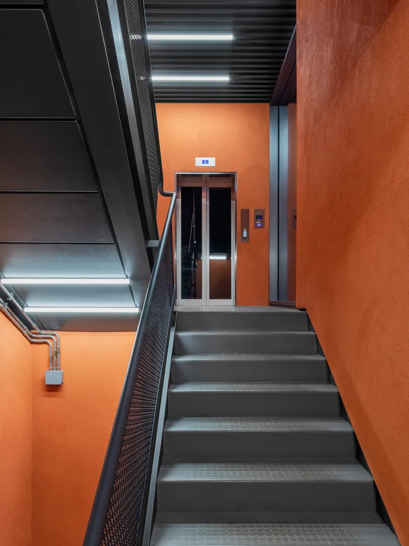 Staircase landing with elevator doors framed by orange walls and black metal detailing
