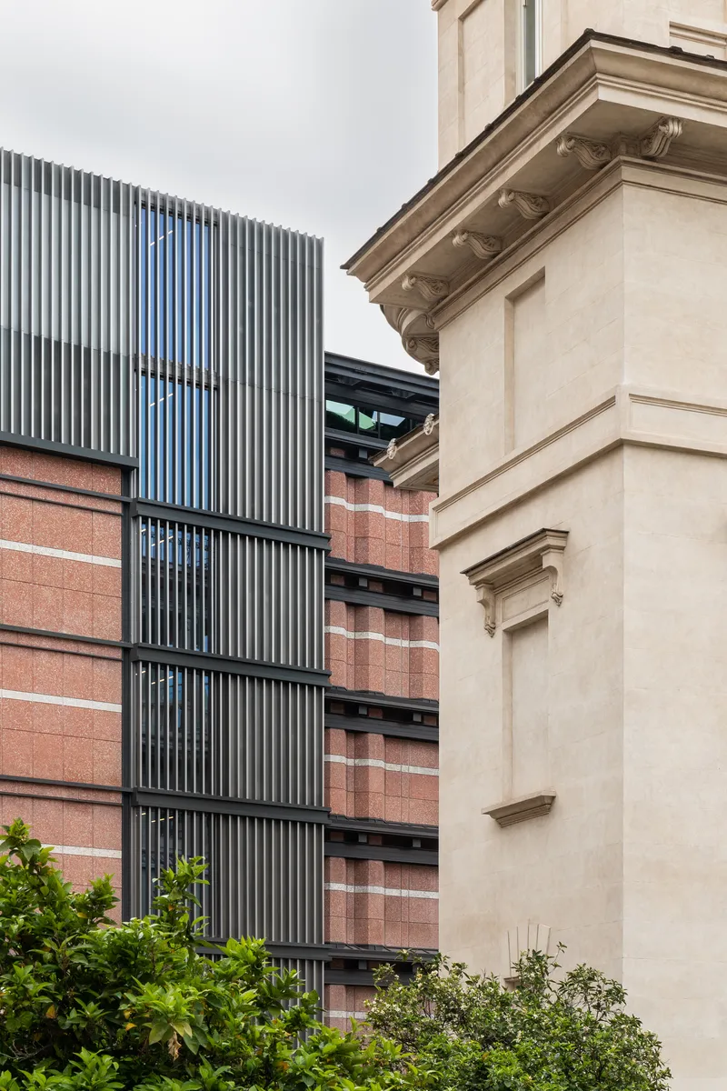 Vertical fin louvres rising beside red brick bands and a rendered heritage corner under overcast skies