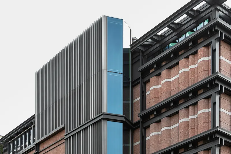Facade detail showing vertical metal fins meeting blue glass cladding and red brick panels with white stripes
