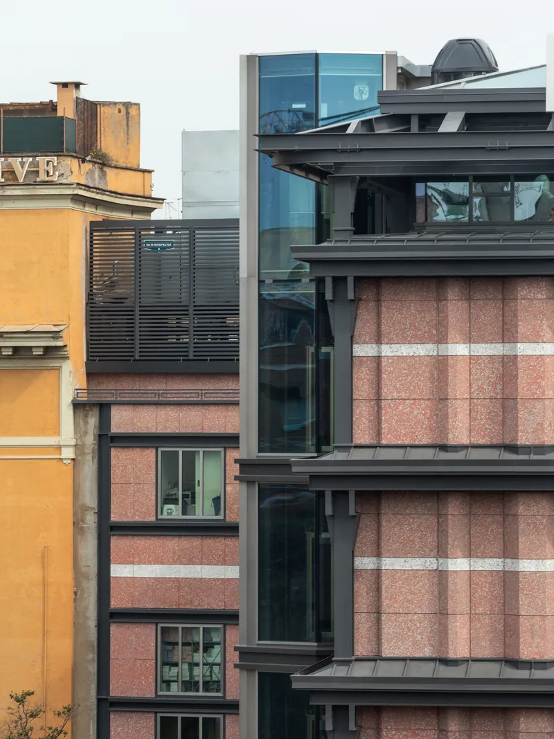 Street elevation with layered balconies, blue glass boxes and weathered ochre heritage building at left