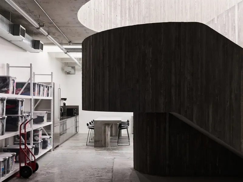 Dark timber clad volume enclosing a dining area beneath exposed concrete ceiling and mechanical ducts