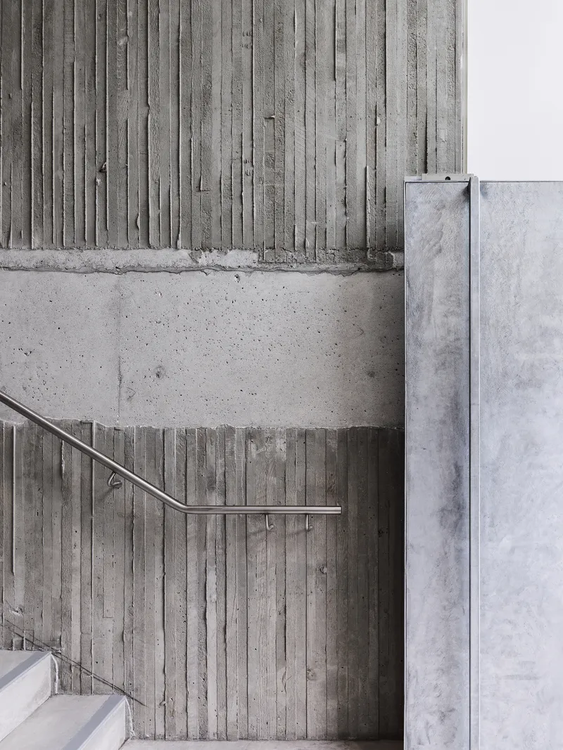 Board-formed concrete wall with stainless steel handrail alongside white painted masonry wall