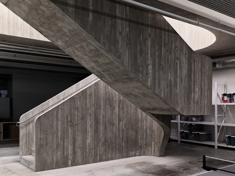 Angled board-formed concrete staircase with vertical planking texture beneath exposed structural slab
