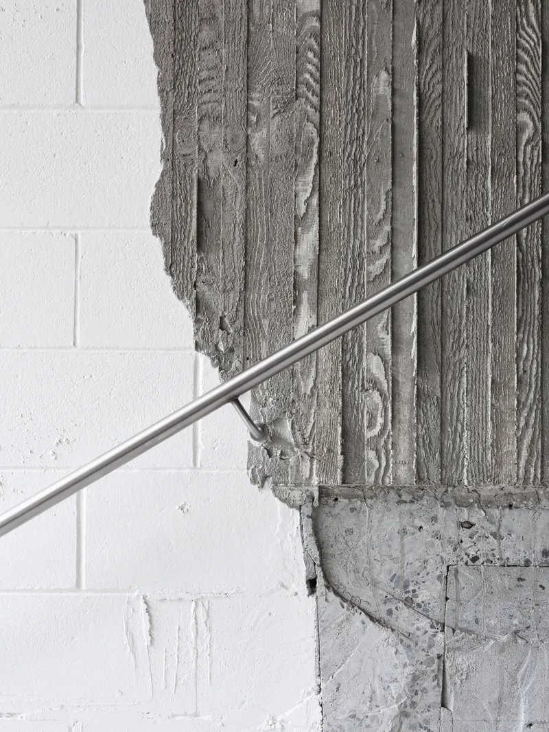 Close-up of board-formed concrete surface showing wood grain texture next to white painted masonry