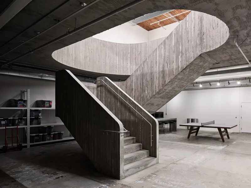 View of the sculptural staircase with metal handrail beneath exposed concrete beams and industrial ceiling
