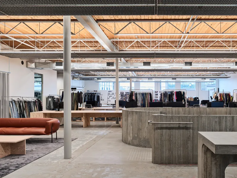 Open retail floor with exposed timber trusses, white steel columns and curved concrete reception desk