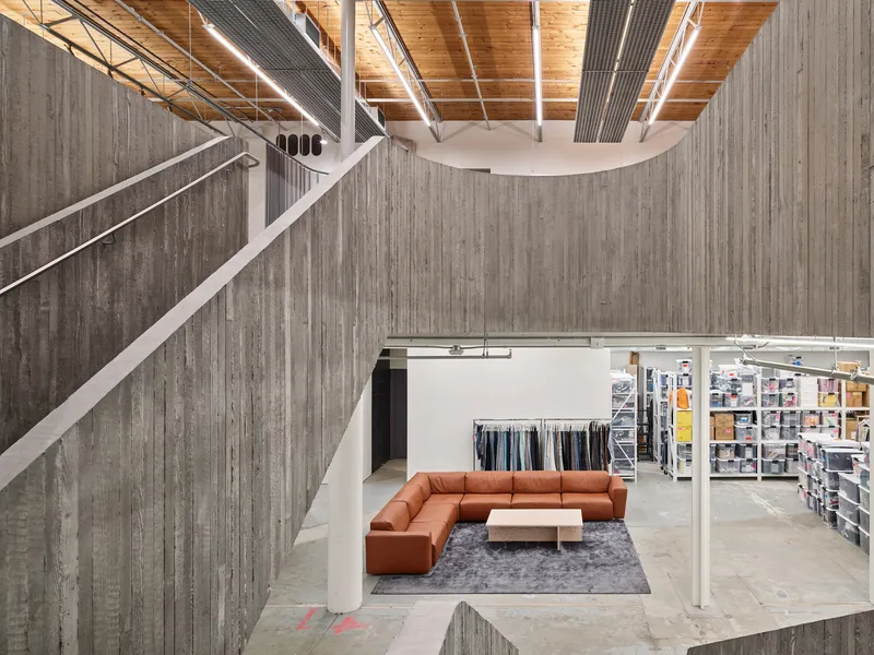 Upper level view showing board-formed concrete wall, timber ceiling and seating area with orange sectional sofa
