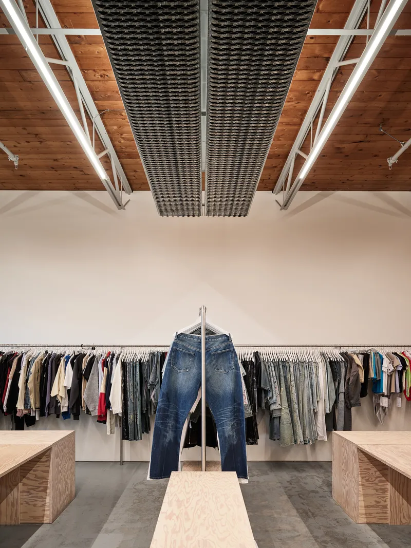 Clothing racks beneath timber ceiling with metal mesh ductwork running between white painted steel trusses