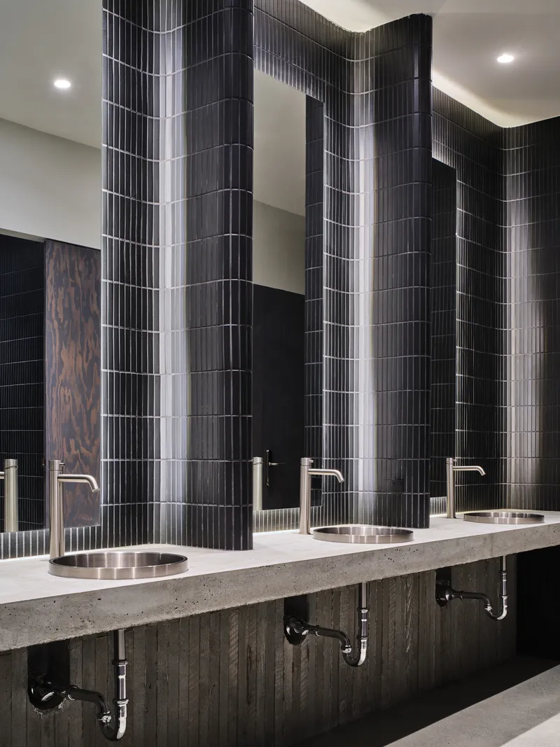 Restroom vanity with terrazzo counter, round metal sinks and vertically ribbed black tile wall panels