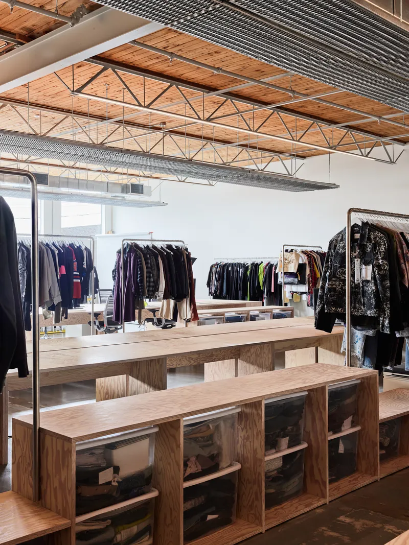 Open retail area with exposed wood trusses, metal deck ceiling and plywood display benches beneath clothing racks