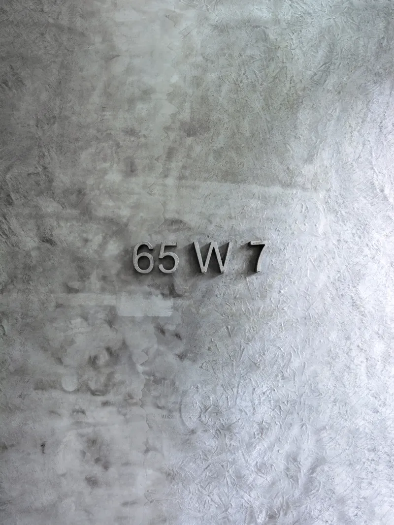 Metallic address numbers mounted on a textured concrete wall with weathered patina