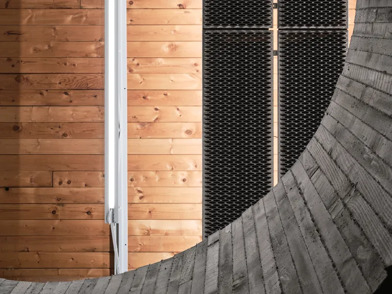 Detail of timber wall cladding meeting black perforated metal panel and grey woven mat