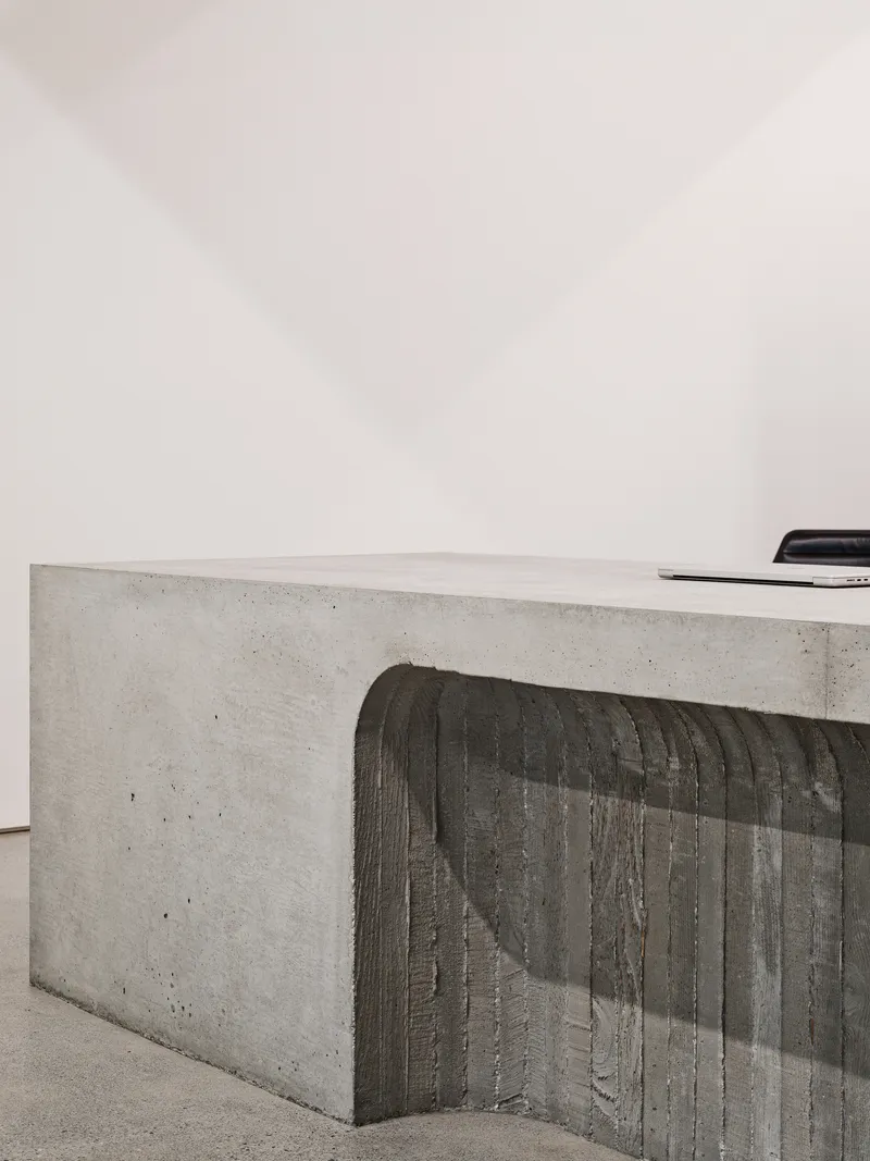 Close-up of board-formed concrete counter with vertical timber texture against a white wall