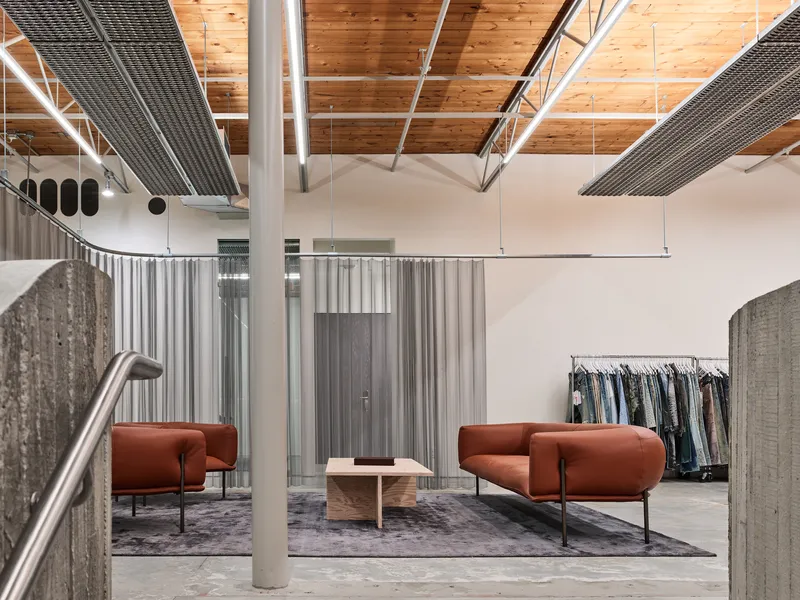 Interior retail space with terracotta lounge chairs on a rug beneath exposed timber ceiling and mesh panels