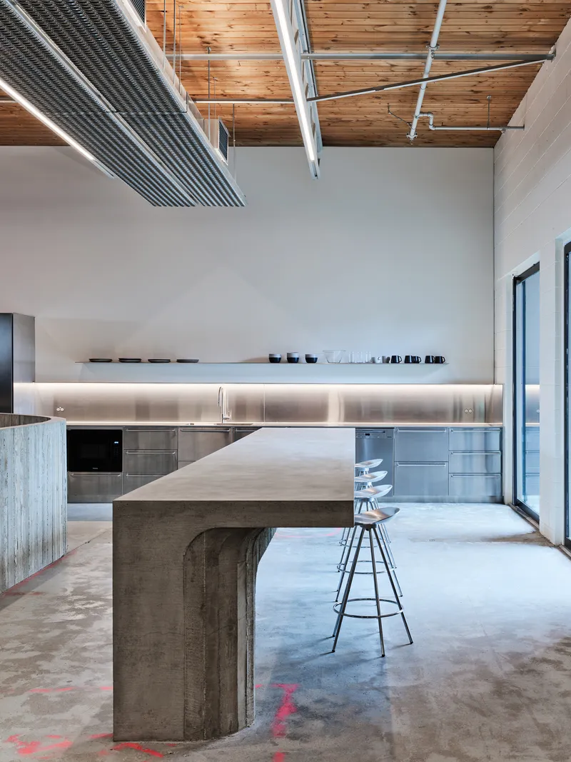 Kitchen with concrete island table and backlit upper cabinet under exposed timber ceiling and conduit